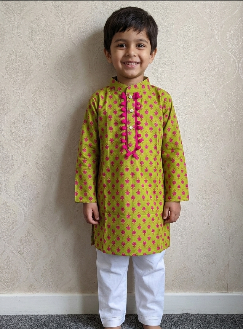 A young boy wearing a green kurta with pink floral motifs and a pink decorative placket, paired with white pants.