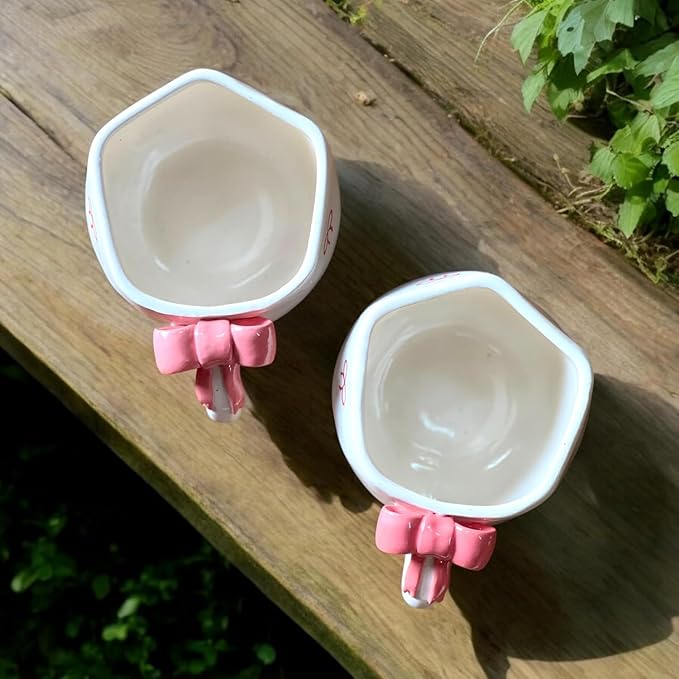 Two small coffee mugs with pink holders on a wooden surface.