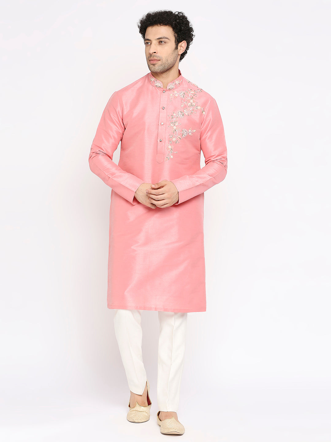 A man modeling a light pink long kurta with silver floral embroidery on the chest, paired with white trousers and beige shoes, against a plain white background.